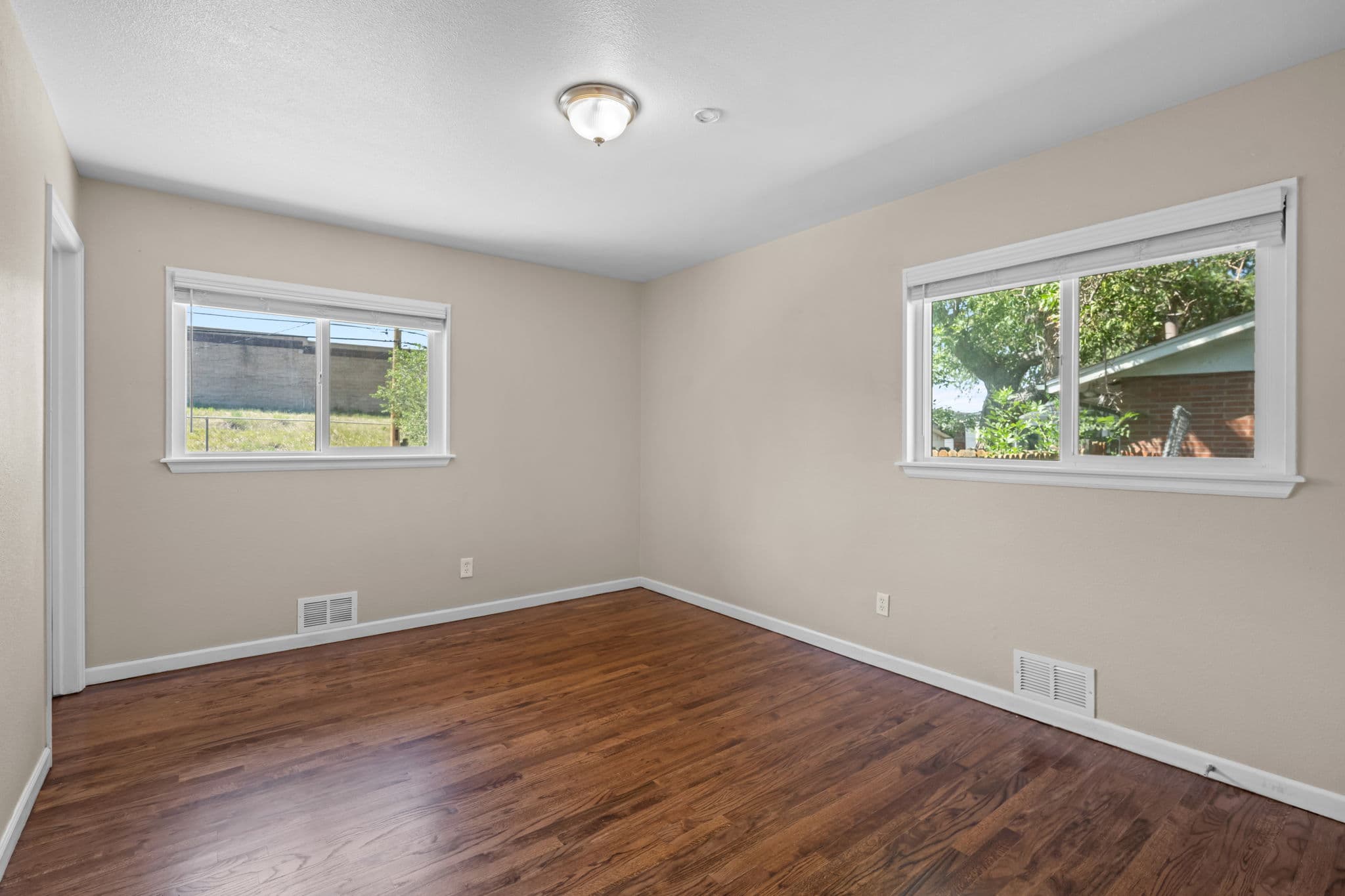 A private bedroom with two windows and hardwood floors